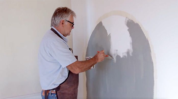 un hombre pinta una pared con una brocha y pintura de color gris