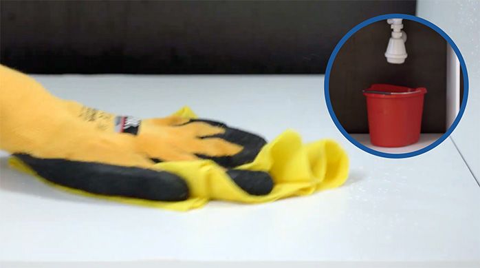 una persona con guantes pasa un paño de fibra para secar la parte de abajo de un lavaplatos que gotea