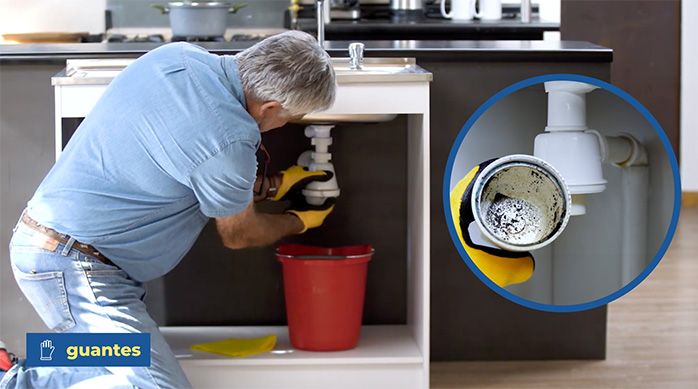 un hombre con guantes desarma el sifón de un lavaplatos de cocina