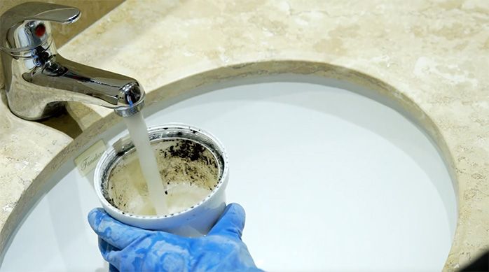 una persona limpiando el sifón de un lavaplatos de cocina en un lavamanos