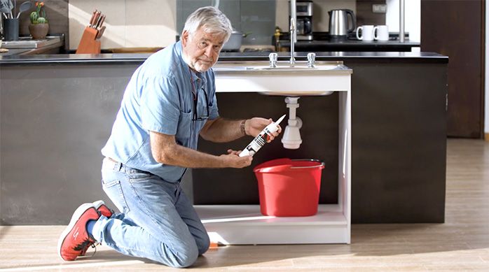 un hombre reparando un lavaplatos que gotea con un sellante