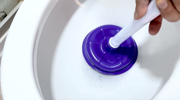 una persona pone un sopapo clásico en la salida de agua de un inodoro para destapar el wc