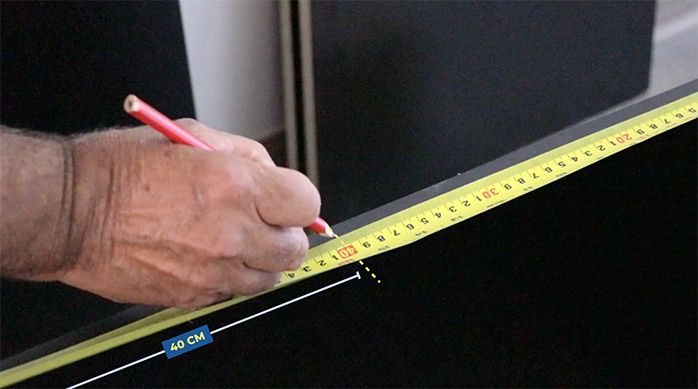 un hombre marca 40 cm con un huincha de medir en el canto de un trozo de melamina