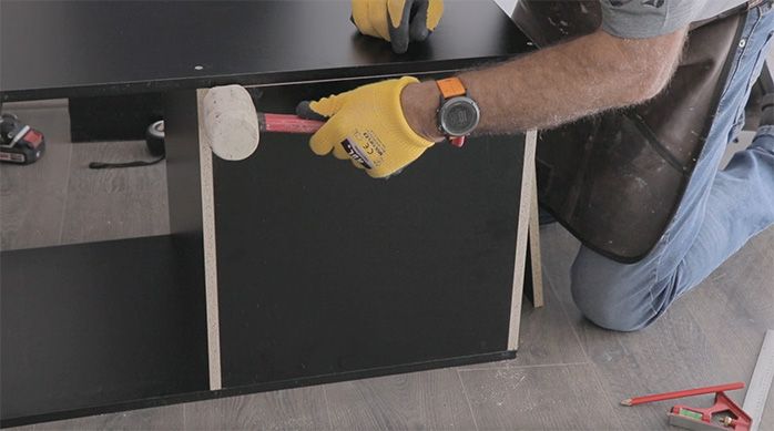 un hombre pone un fondo en el mueble gamer horizontal y lo ajusta con un martillo de goma