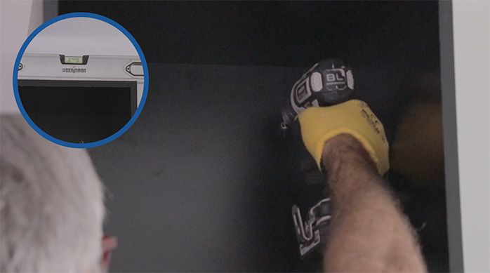un hombre marca a través de la perforación del fondo del mueble gamer el lugar de fijación en el muro