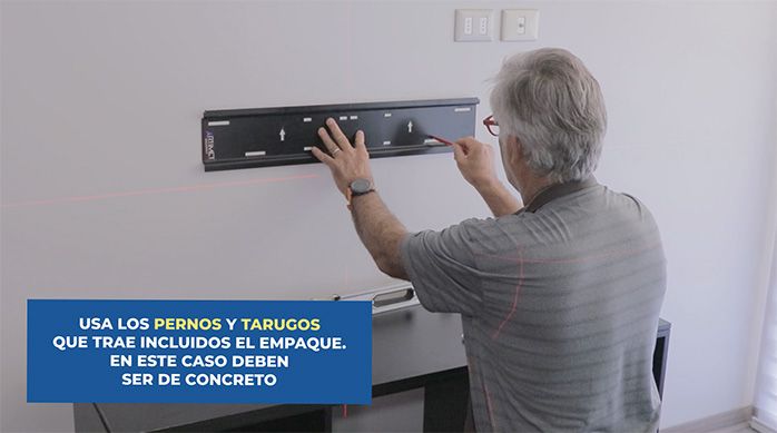 un hombre marca el lugar de las fijaciones a través de los agujeros del soporte para tv