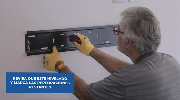 un hombre marca las fijaciones del soporte para tv a través de sus agujeros