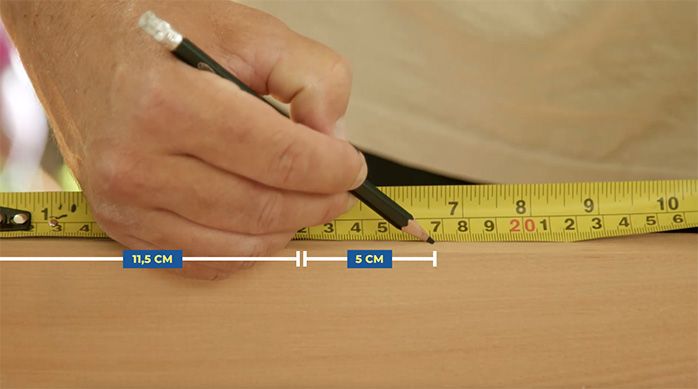 una persona marca con un lápiz dos fijaciones en un trozo de madera con una huincha de medir