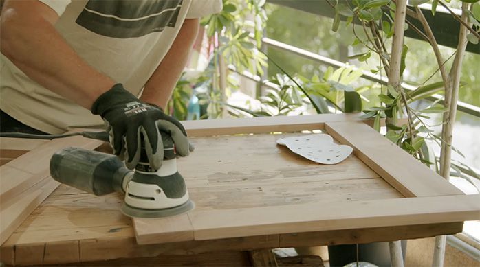 un hombre lija las partes de la mesa plegable de madera con una lijadora roto orbital