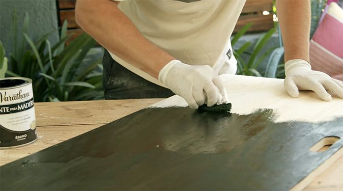 un hombre aplica tinte para madera color ébano en la cubierta de la mesa plegable de madera