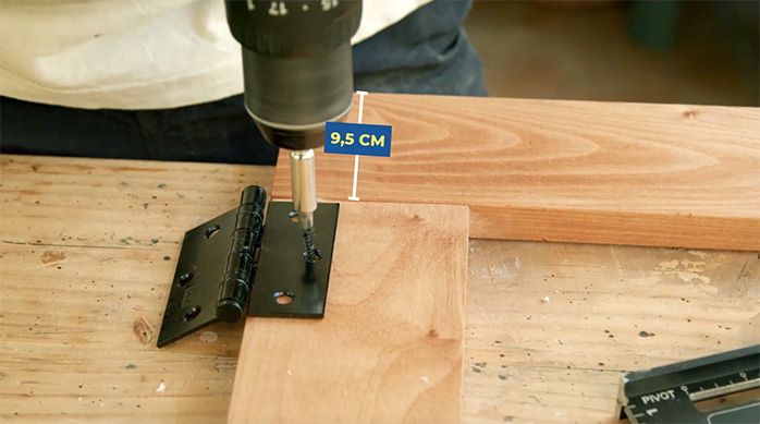 un hombre atornilla las bisagras de la mesa plegable de madera