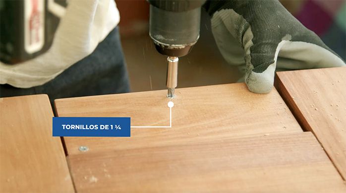 un hombre atornilla unos trozos de madera en la base de la estructura de la mesa plegable de madera