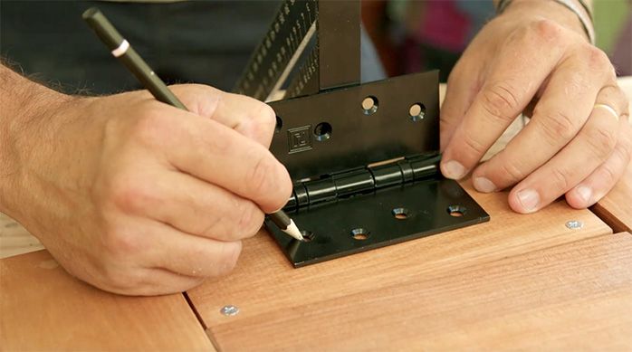un hombre marca la posición de las bisagras en la base de la mesa de madera