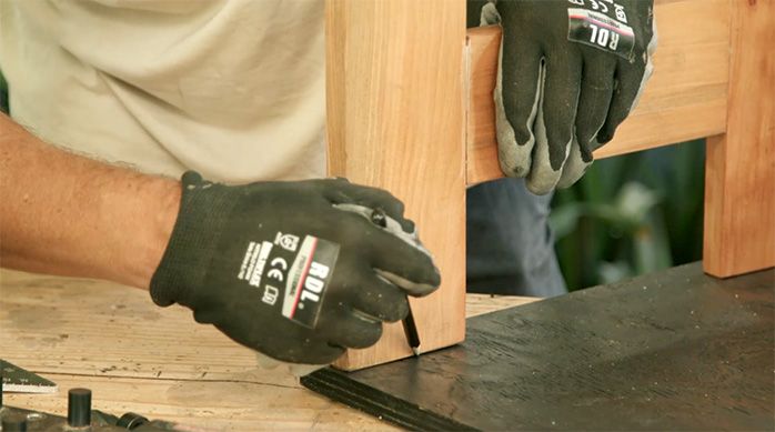 un hombre marca el contorno de una de las patas de la mesa plegable de madera en la cubierta