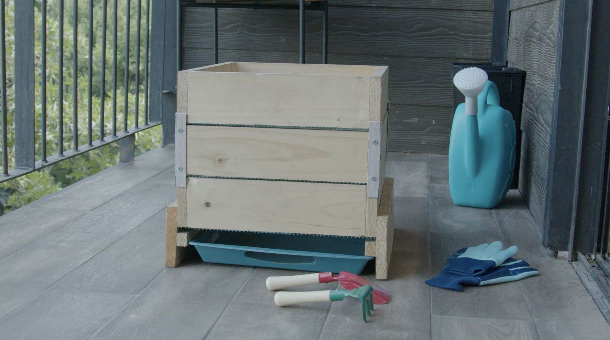 compostera para departamento con unos guantos, regadera y herramientas de jardinería para aprender a hacer compost