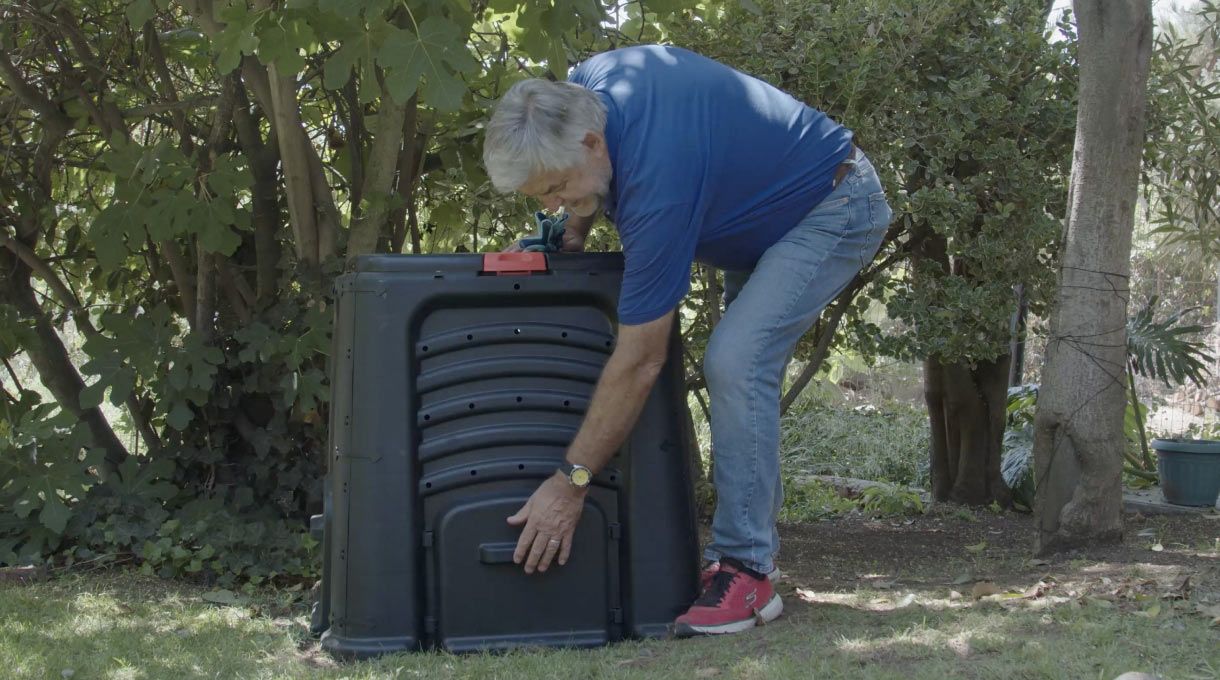 un hombre muestra la tapa de una compostera de plástico para hacer compost en casa