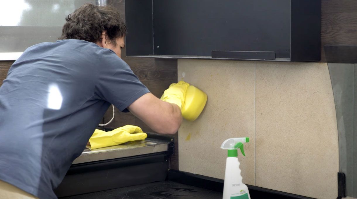 un hombre limpia la pared de una cocina con una esponja amarilla grande