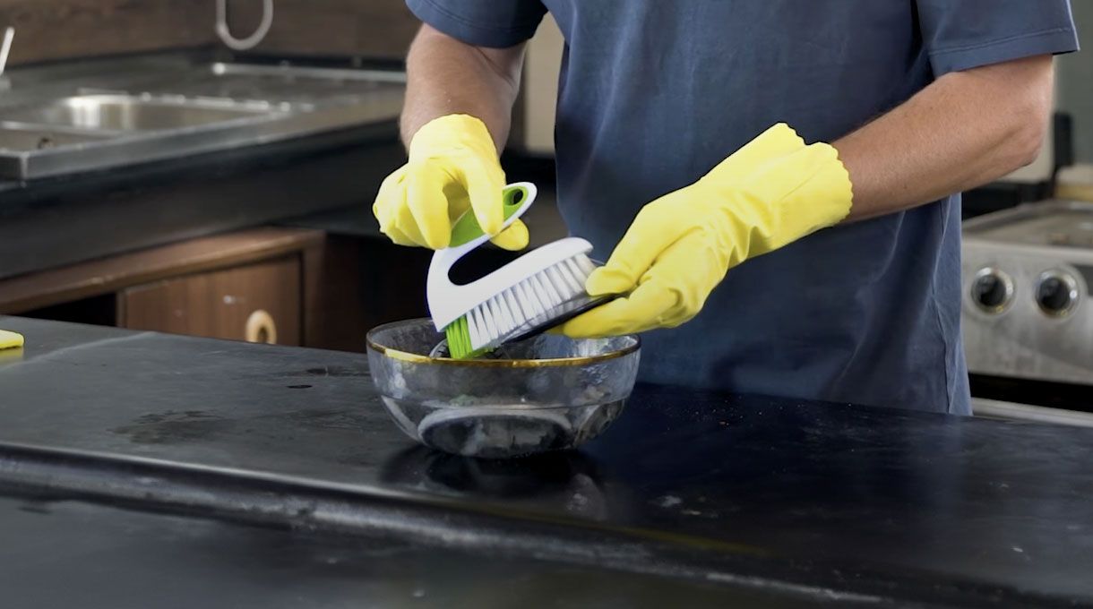 un hombre con guantes limpia los quemadores de una cocina con una escobilla