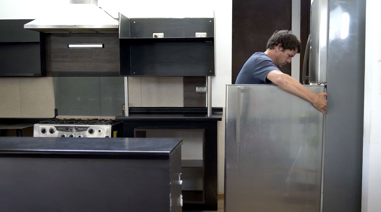 un hombre mueve el refrigerador de la cocina para limpiar detrás