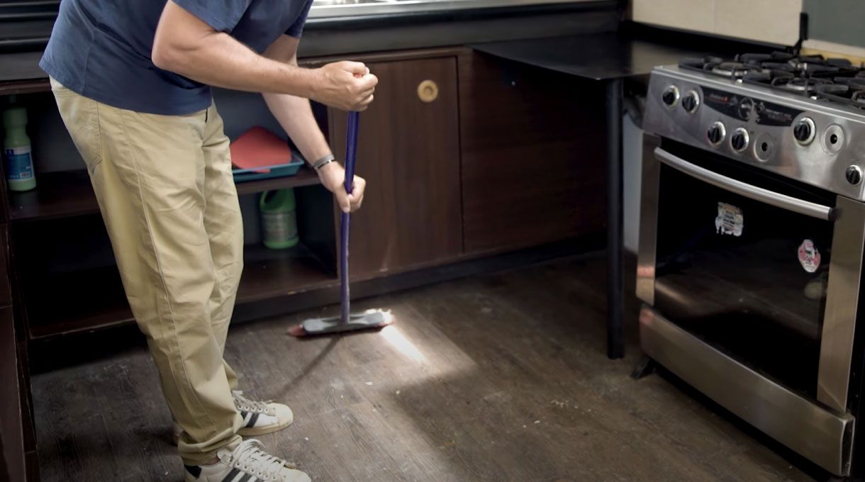 un hombre barre el piso de la cocina con una escoba