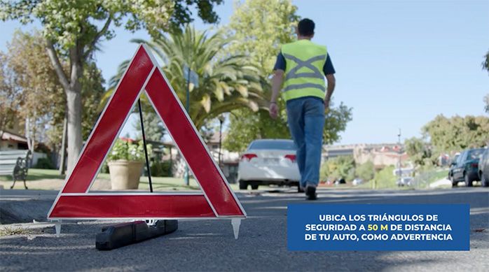 un hombre camina hacia su auto blanco luego de poner un triángulo de seguridad para cambiar los neumáticos