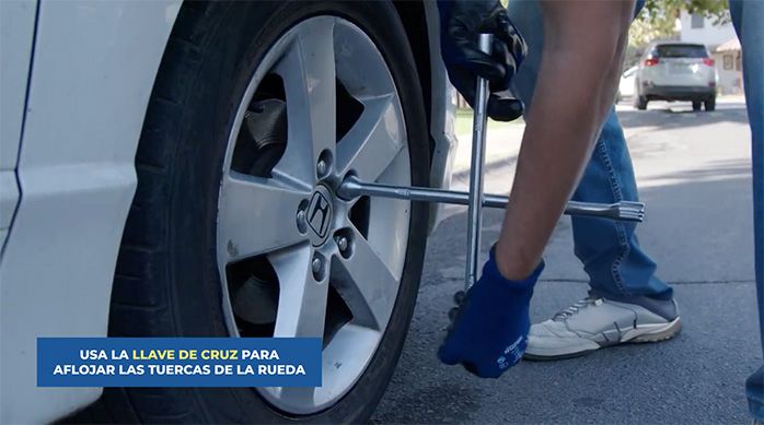 una persona usa una llave de cruz para desmontar un neumático