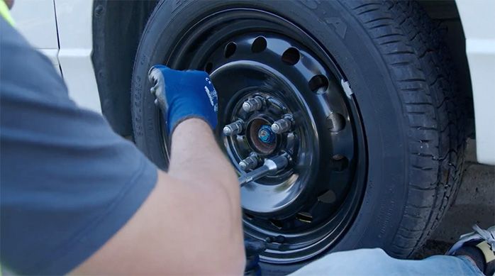 un hombre usa una llave para apretar los pernos de un neumático de repuesto