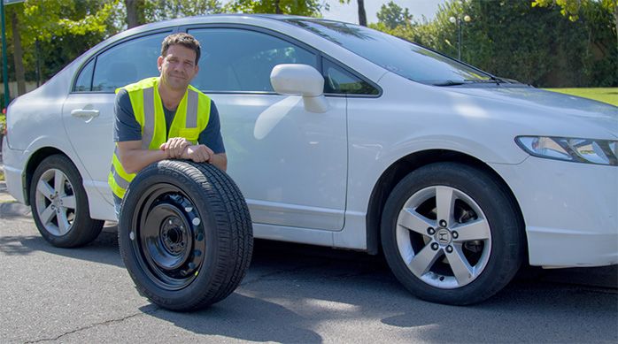 un hombre con chaleco reflectante sostiene un neumático al frente de un auto blanco