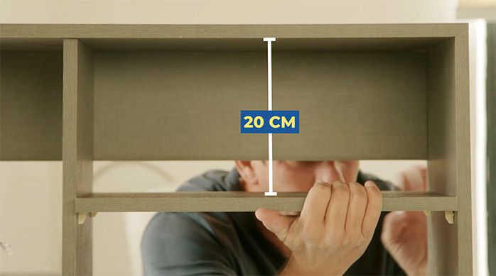 un hombre pone una repisa a 20 cm desde la parte superior del mueble organizador