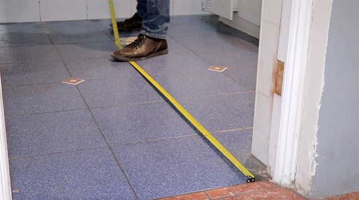 un hombre mide las dimensiones del piso de un baño con una huincha de medir
