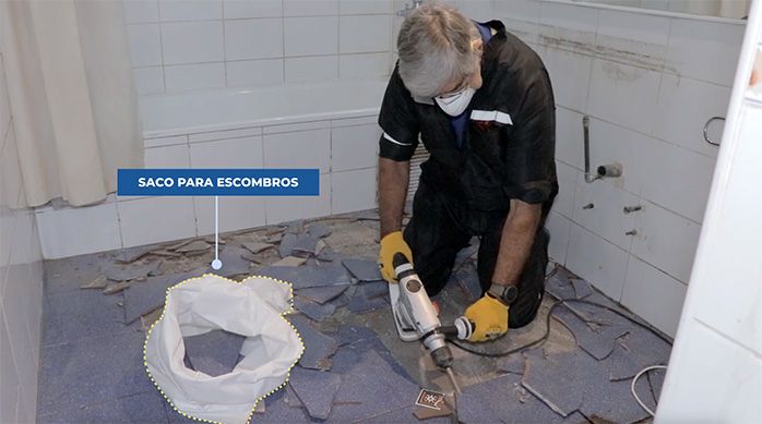 un hombre rompe la cerámica del piso de un baño con un rotomartillo y pone los escombros en un saco para escombros