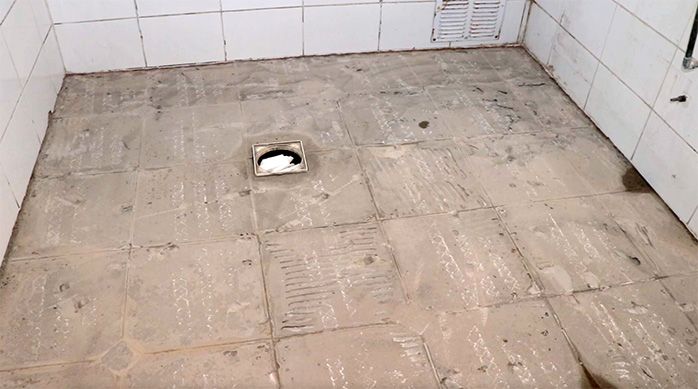 piso de baño limpio sin cerámicas ni revestimientos, con un hoyo de desagüe tapado con una bolsa para escombros