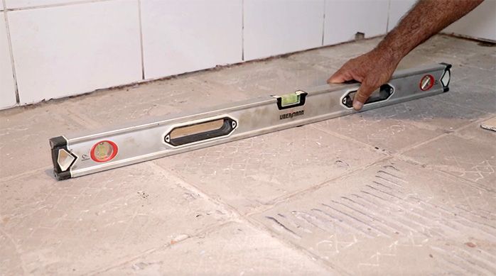 un hombre verifica el nivel del piso del baño con un nivel de burbuja