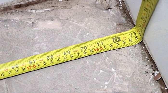 una huincha de medir doblada en la unión del piso del baño y el muro