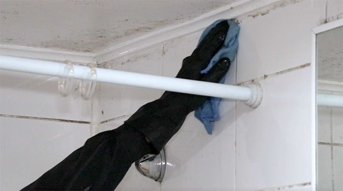 un hombre limpia el muro de un baño con una solución de cloro para eliminar los hongos