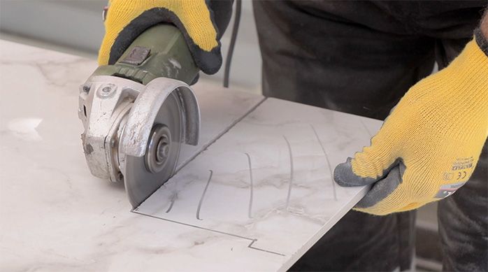 un hombre corta el porcelanato con un esmeril angular