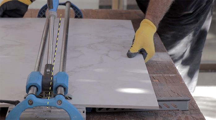 un hombre corta el porcelanato de piso con una cortadora de cerámica
