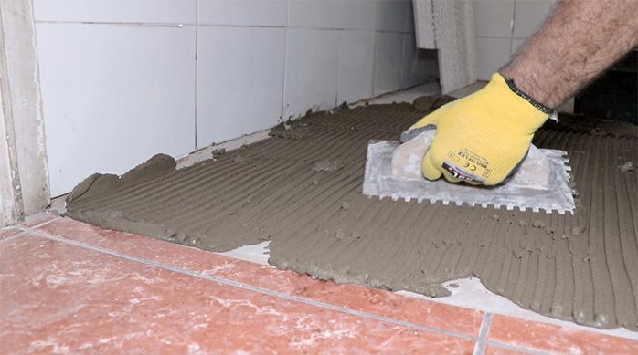 un hombre esparce el pegamento para porcelanato con una llana dentada