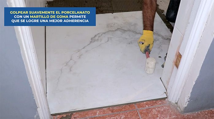 un hombre golpea con un martillo de goma la plancha de porcelanato para baños para asentarla en el piso