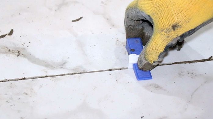 un hombre pone unas cuñas niveladoras en la unión entre planchas de porcelanato