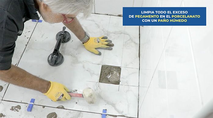 un hombre pega el corte de porcelanato con pegamento para porcelanato y luego lo golpea suavemente con un mazo de goma
