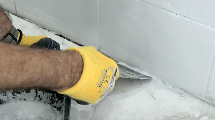 un hombre aplica el fragüe en la unión del porcelanato de piso con el muro usando una espátula flexible
