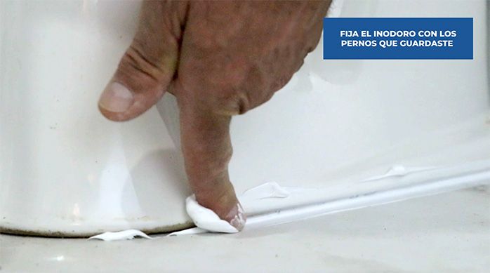 un hombre pasa el dedo para emparejar un cordón de silicona que une el inodoro al piso del baño