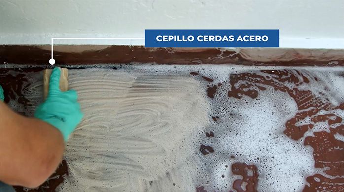 un hombre usa un cepillo con cerdas de acero para limpiar el piso de cemento