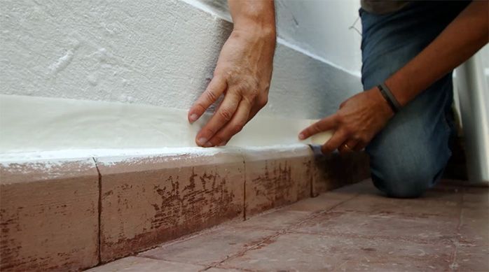 un hombre pone cinta de enmascarar para proteger el muro del espacio en donde se va a pintar un piso de cemento