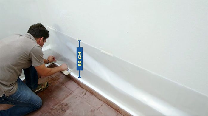 un hombre pone un plástico protector de 50 cm en el muro para protegerlo al pintar un piso de cemento