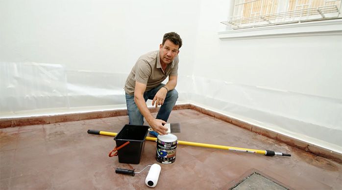 un hombre presenta los materiales necesarios para pintar un piso de cemento