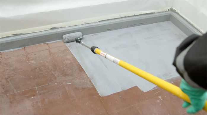 un hombre pinta un piso de cemento con un rodillo y un extensor para rodillo