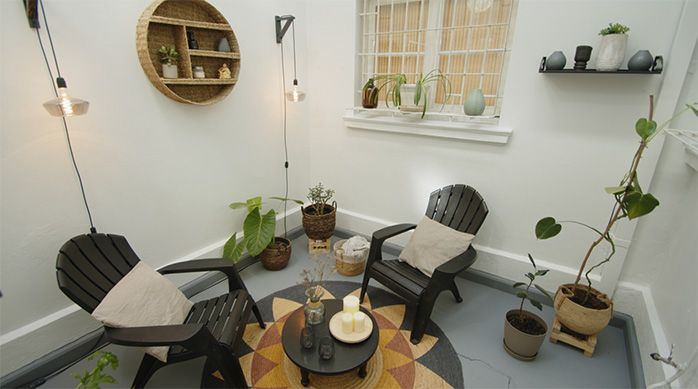 un patio techado con sillas, una mesa de centro, repisas y plantas con su piso de cemento recién pintado
