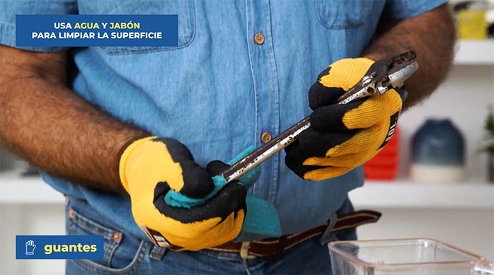 un hombre sostiene una llave inglesa oxidada y la limpia superficialmente con un paño